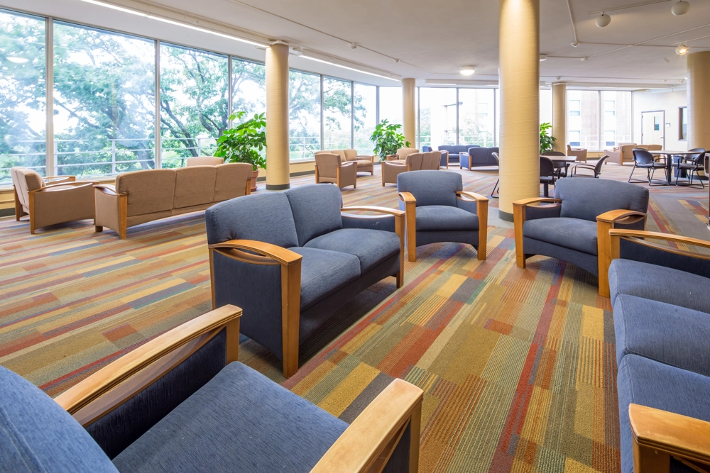 common area in a university dorm with seating areas including couches and chairs and tables with chairs